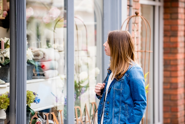 A woman shopping at a flower shop, admiring floral arrangements through a glass window.