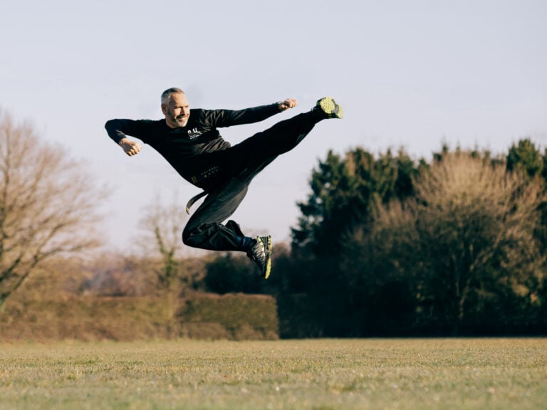 Dynamic martial arts kick captured outdoors during daylight.