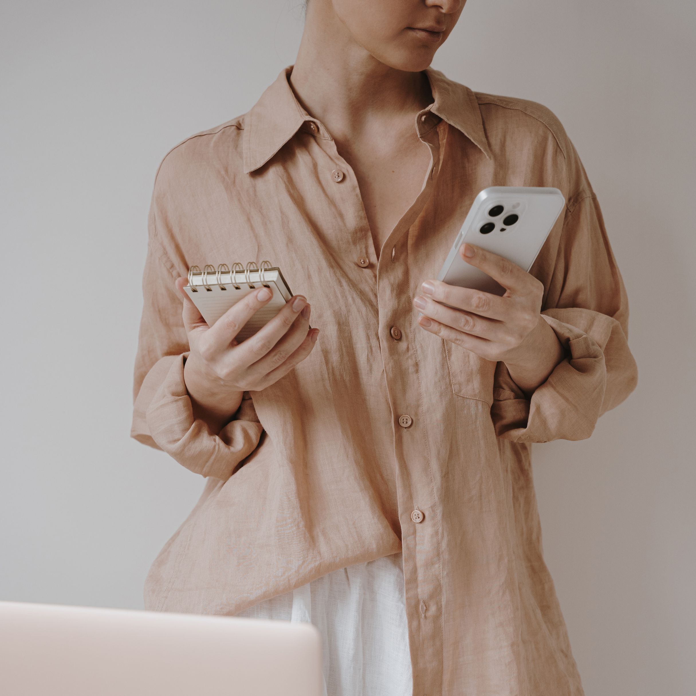 Professional female image editing in neutral tones, modern smartphone, and notepad.